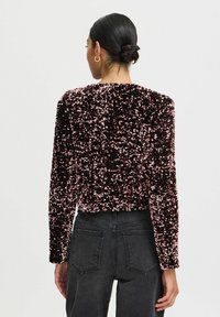 Sort og lyserød pailletbesat cropped jakke med lange ærmer, struktureret overflade og rund halsudskæring, parret med højtaljede mørke jeans.
