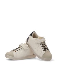 Zapatillas blancas con una puntera beige texturizada, cordones con estampado, una correa de velcro y un acento brillante en el talón negro. Presenta agujeros de ventilación.