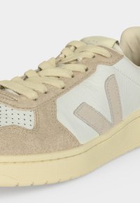 Baskets décontractées beige et blanches avec panneaux en daim et cuir, détails perforés, lacets crème et semelle épaisse en caoutchouc.