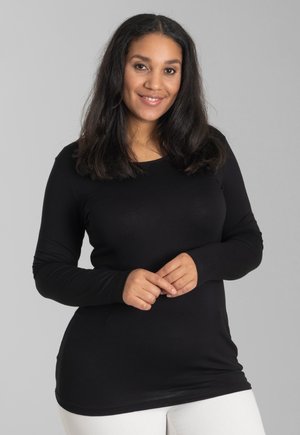 Zwarte longsleeve top van rekbaar materiaal, met een ronde halslijn en een nauwsluitend ontwerp, gecombineerd met witte broek.