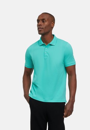 Turquoise polo shirt met korte mouwen, drieknopen placket en een gladde textuur, gecombineerd met donkere broeken. Geen patronen of accenten.
