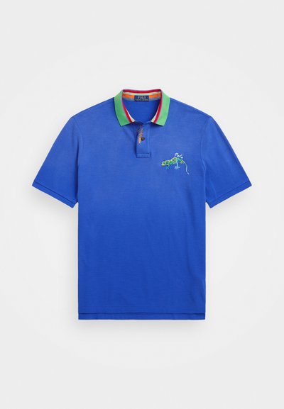 Polo azul com gola verde, com detalhes em vermelho e branco, e design de lagarto bordado no lado esquerdo do peito. Mangas curtas.