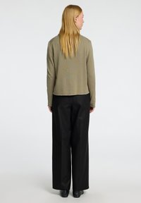 Olivno zelena kratka jakna z teksturirano pleteno zasnovo, v kombinaciji s črnimi širokimi hlačami. Gladek material s sproščenim krojem.