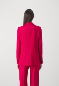 Fuksia bleiseri muotoiltu istuvuudella, notkottu kaulus ja pitkät hihat. Sileä kangas, keskiselkäsauma, yhdistetty yhteensopiviin housuihin.
