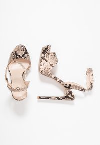 Sandales à talons hauts avec un motif en peau de serpent beige et noir, design à bout ouvert, et fines lanières autour de la cheville avec un talon aiguille.