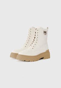 Botas de tornozelo brancas com atacadores, com uma sola bege robusta, apresentando um acabamento metálico brilhante de um lado e um material semelhante a couro suave.