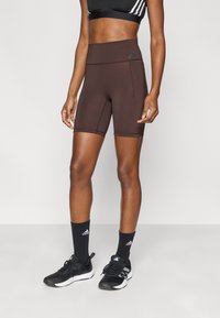 Καφέ ψηλόμεσα ποδηλατικά σορτς από ελαστικό ύφασμα. Διαθέτουν πλαϊνή τσέπη και ανάγλυφο λογότυπο στη μέση.