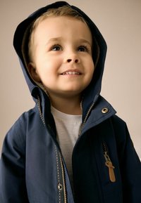 Veste à capuche marine avec fermeture éclair et accents en cuir. Présente un intérieur doux et des poches avant. Tissu texturé, coupe moderne.