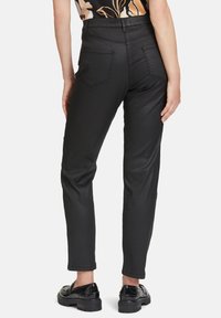 Schwarze, taillierte Hosen mit glatter Textur, Fünf-Taschen-Design und geraden Beinen. Getragen mit glänzenden, schwarzen Schnürschuhen.