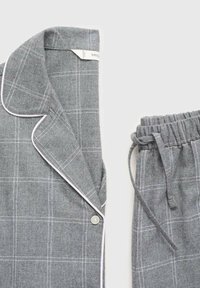 Conjunto de pijama de cuadros grises hecho de tela suave. Incluye una camisa con botones y ribete blanco, y pantalones con cintura elástica a juego.