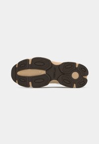 Shoe outsole featuring a brown rubber design with textured traction patterns, contrasting light and dark elements, and brand logo inscription.