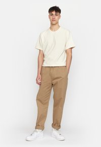 Camiseta de manga corta color crema con cuello redondo, combinada con pantalones de cintura elástica marrón claro, puños doblados y zapatillas blancas.