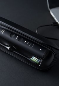Schwarze elektrische Zahnbürste in einem eleganten Etui. Das Gerät verfügt über einen Ein-/Ausschalter, fünf Modusanzeigen und einen abnehmbaren Bürstenkopf mit weichen Borsten.