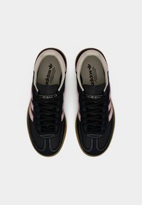 Ζευγάρι μαύρα αθλητικά παπούτσια Adidas με ροζ ρίγες και σόλες καουτσούκ, από ψηλά σε λευκό αφαιρετικό φόντο.