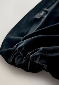 Czarna aksamitna tkanina o zgromadzonej strukturze, prezentująca delikatny połysk. Krawędzie są lekko postrzępione, co podkreśla puszystą jakość materiału.