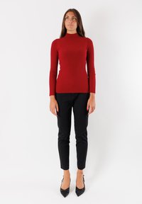 Maglione a collo alto rosso a coste abbinato a pantaloni neri slim fit e décolleté neri a punta, creando una silhouette aderente.