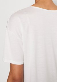 Biała koszulka z krótkim rękawem o luźnym kroju i szerokim dekoltem. Miękka, lekka tkanina o lekko teksturowanej powierzchni.