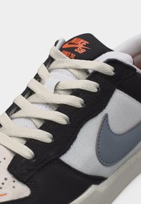 Nike SB Force 58 tossud valgete paeltega, must-valge ülaosaga, halli S-kujuga ja oranži Nike SB logoga mustal keelel.