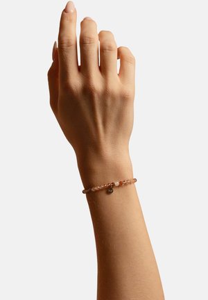 Rosenquarz-Perlenarmband mit einem runden Metallanhänger, das eine durchscheinend rosa Farbe, eine glatte Textur und ein filigranes elastisches Banddesign aufweist.