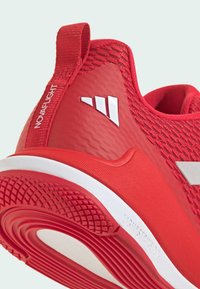 Baskets de sport rouges avec une tige en mesh texturé, une marque bien visible et une semelle intermédiaire blanche. Elles disposent d'une semelle externe en caoutchouc avec un grip à motifs.