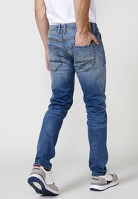 Mismo azul deslavado, jeans de corte ajustado con bolsillos traseros y detalles de costura. Combinados con zapatillas deportivas grises y blancas.