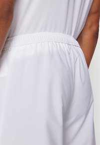 Shorts attivi bianchi con vita elasticizzata e tessuto texturizzato, che mettono in risalto una finitura liscia e un design funzionale.