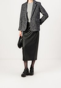 Hahnentritt-Blazer mit Kerbkragen, grauem Oberteil, schwarzem Ledermidirock, schwarzen klobigen Absätzen und einer schwarzen Handtasche. Details aus strukturiertem Stoff.