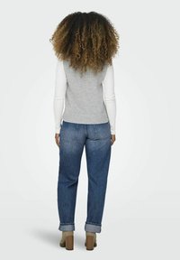 Grijs ribgebreid vest met witte lange mouwen, gedragen met blauwe high-waisted jeans en beige hoge enkellaarsjes. Gelaagd haar dat onder de schouders valt.