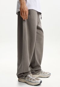 Grijze, loszittende sweatpants met een verstelbare tailleband, gemaakt van zachte stof; gecombineerd met lichtgekleurde, ademende hardloopschoenen.