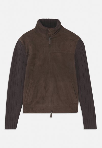 Ruda zomšinė striukė su papirinta megzta rankovėmis, aukštu apykakle, priekiniais užtrauktukais ir dviem šoninėmis kišenėmis. Minkšta tekstūra su kontrastiniais elementais.