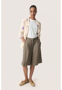 Cremefarbener Blazer mit Blumenmuster, weißes T-Shirt und olivgrüne weit geschnittene Shorts. Braune Schuhe mit Schnürung. Lässiges Outfit.