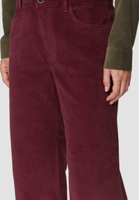 Pantalons en velours côtelé bordeaux à jambes larges, avec texture côtelée et deux poches latérales. Associés à une chemise verte à manches longues.