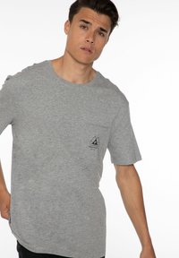 Grijze katoenen t-shirt met korte mouwen, ronde hals en een borstzakje aan de linkerkant met een zwart logo ontwerp.