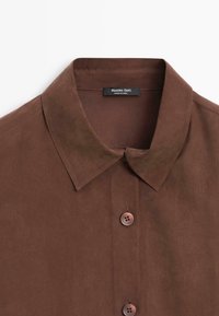 Camicia collare marrone realizzata in tessuto liscio, con due bottoni e un'etichetta sul colletto. Design semplice con un taglio classico.