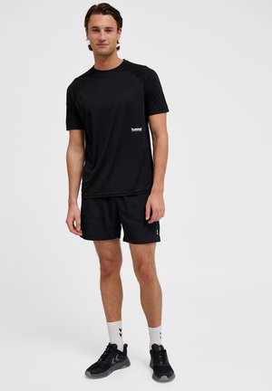 Zwarte sportieve t-shirt met korte raglanmouwen, gladde textuur, gecombineerd met bijpassende zwarte shorts. Accessoires omvatten zwarte sneakers en witte sokken.
