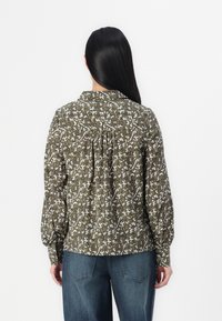 Grønn bluse med blomstermønster, samlede detaljer bak, lange ermer og krage, sammen med blå denimbukser.