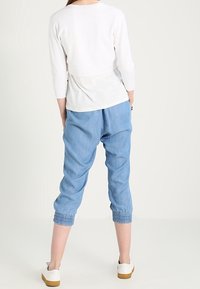 Top blanco recortado de manga larga combinado con pantalones azul claro de puños elásticos y taperados; llevado con zapatos blancos sin cordones.