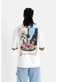 Vit t-shirt med kort ärm som har en färgglad illustration av en vinflaska och frukt på en tallrik, med abstrakta element och text.