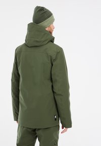 Grüne wasserdichte Jacke mit Kapuze, aus glattem Material. Verfügt über einen Reißverschluss und ein Logo-Patch am Saum. Einfaches, modernes Design.