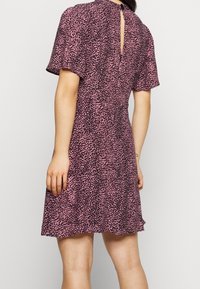 Šaty s krátkým rukávem z růžové látky s černým zvířecím vzorem, s detailem ve tvaru klíčové dírky na zádech a rozšířeným zakončením.