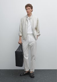 Cremefarvet linnedjakke, hvid t-shirt og hvide bukser med sorte loafers. Bærer en sort tote bag; minimalistisk design og rene linjer.