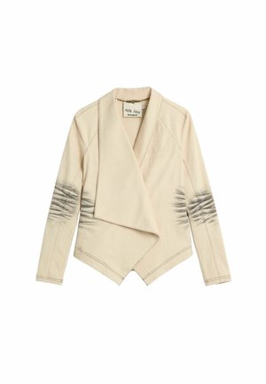 Beež pikkade varrukatega jakk, millel on langeva kujundusega avatud esiküljega, varrukatel musta lipsuvärvi detailid ja servade ümber nähtavad õmblused.