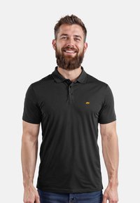Polo nero realizzato in un tessuto liscio e traspirante. Presenta una pattina con tre bottoni e un piccolo logo di un orsetto arancione sul lato sinistro del petto.