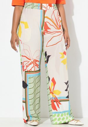 Szerokie spodnie o nogawkach z kolorowymi abstrakcyjnymi kwiatowymi i geometrycznymi wzorami, noszone z białymi, spiczastymi balerinami oraz pomarańczową bluzką.