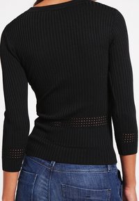 Schwarzes, langärmliges Rippoberteil mit figurbetontem Schnitt, strukturierten Akzenten und Ausschnitten an Taille und Ärmelsäumen.