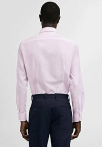 Lichtroze blouse met lange mouwen en een klassieke kraag, gecombineerd met dondernavy broek. De blouse heeft knoopsluiting bij de mouwen en een soepele textuur.