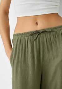 Kalhoty z lehké crinklované látky olivové barvy s elastickým pasem a detaily na šňůrku; kapsy po obou stranách.