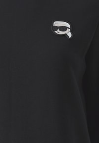 T-shirt in cotone nero con un piccolo logo ricamato grigio e bianco che rappresenta un volto stilizzato con occhiali da sole sul petto.