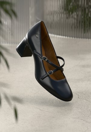 Talons en cuir verni noir avec un bout arrondi, comportant deux sangles décoratives avec boucles. Surface texturée, talon moyen.