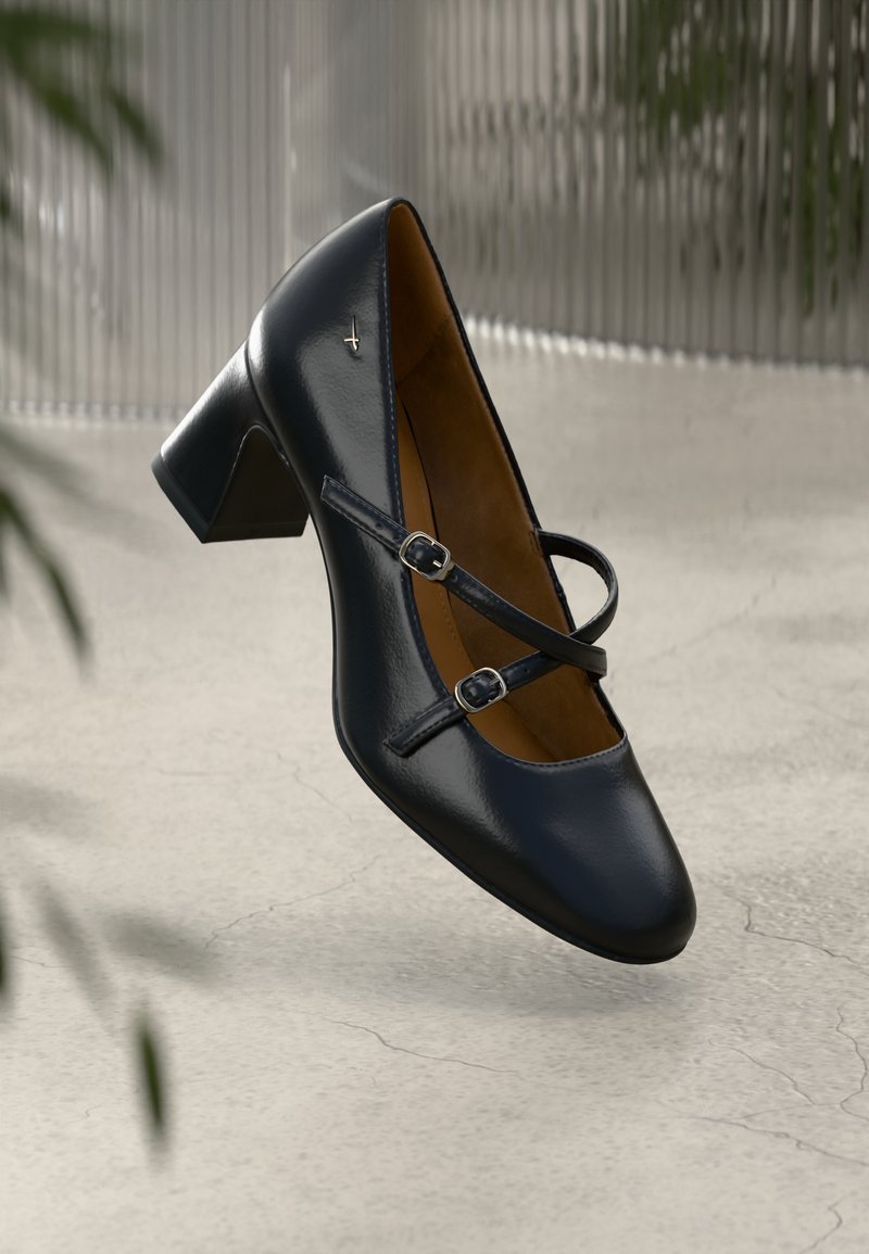 Μαύρο παπούτσι με γυαλιστερή επιφάνεια και στρογγυλή μύτη, διαθέτοντας δύο διακοσμητικές λουρίδες με αγκράφες. Υφασμάτινη επιφάνεια, μεσαίο τετράγωνο τακούνι.